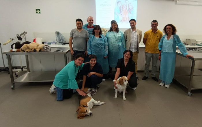 Um grupo de formandos posa para a foto juntamente com o pessoal técnico de uma clínica veterinária. Estão numa sala de tratamento de animais. Na imagem, estão também dois cães.